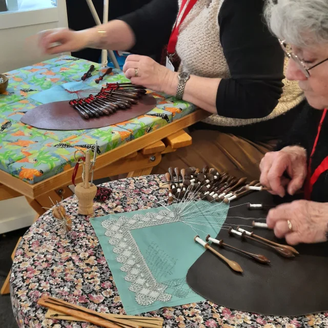 Gros plan des mains de dentellières travaillant sur un carreau avec des fuseaux